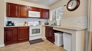 A kitchen with wooden cabinets, a white stove, a microwave, and a clock on the wall. - Brighton House - Walk to Metro (Seattle)