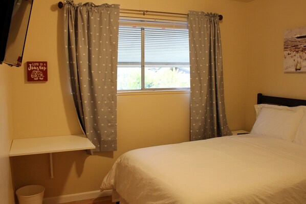 A bedroom with a bed, a window with curtains, a bedside table, and a wall-mounted shelf. - Brighton House - Walk to Metro (Seattle)