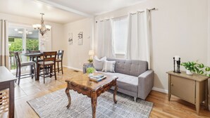 A living room with a grey sofa, wooden coffee table, dining table with chairs, and a small cabinet. - Brighton House - Walk to Metro (Seattle)