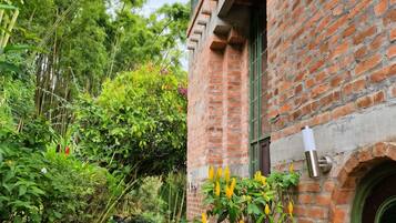 A brick building with a stone pathway leading to a door, surrounded by lush greenery and a dog.