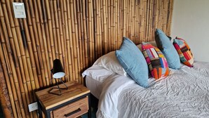 A neatly arranged bedroom with a bamboo wall, a bedside table with a lamp, and a bed with multiple pillows. - Casa Tien (Salento)