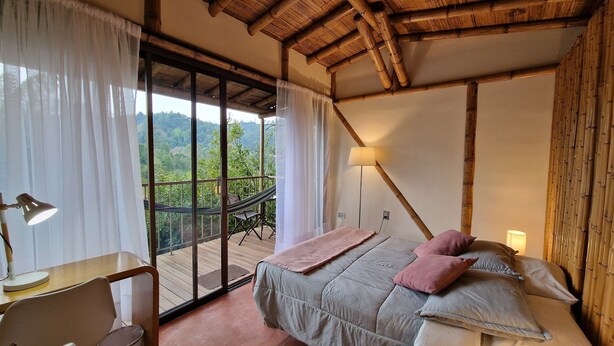 A bedroom with a large window, a bed with pillows, a desk with a lamp, and a view of the outdoors. - Casa Tien (Salento)