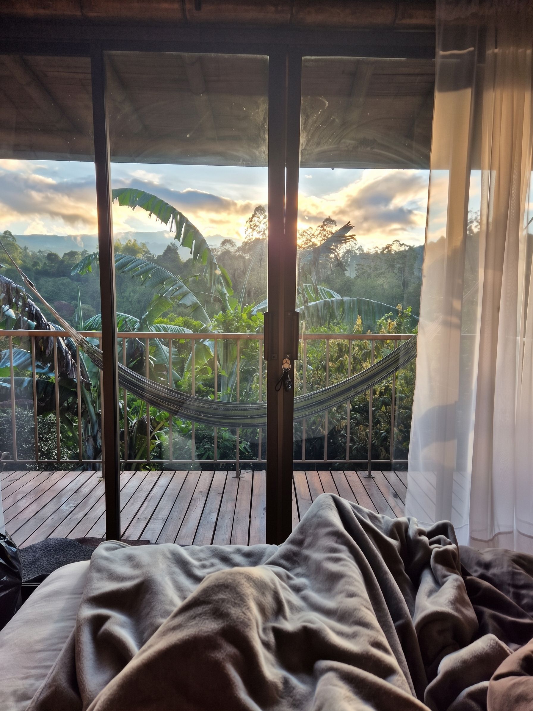 A room with a bed, a hammock, and a view of a landscape with trees and mountains.