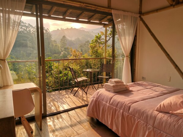 Una habitación con una cama, una mesa y una silla. Cuenta con un balcón y vistas a montañas y árboles.