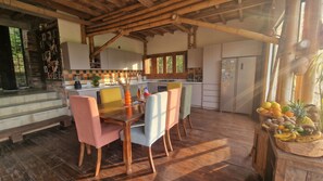 Una cocina moderna con armarios de madera, un comedor con mesa y sillas de madera, y una cesta de frutas a la derecha.