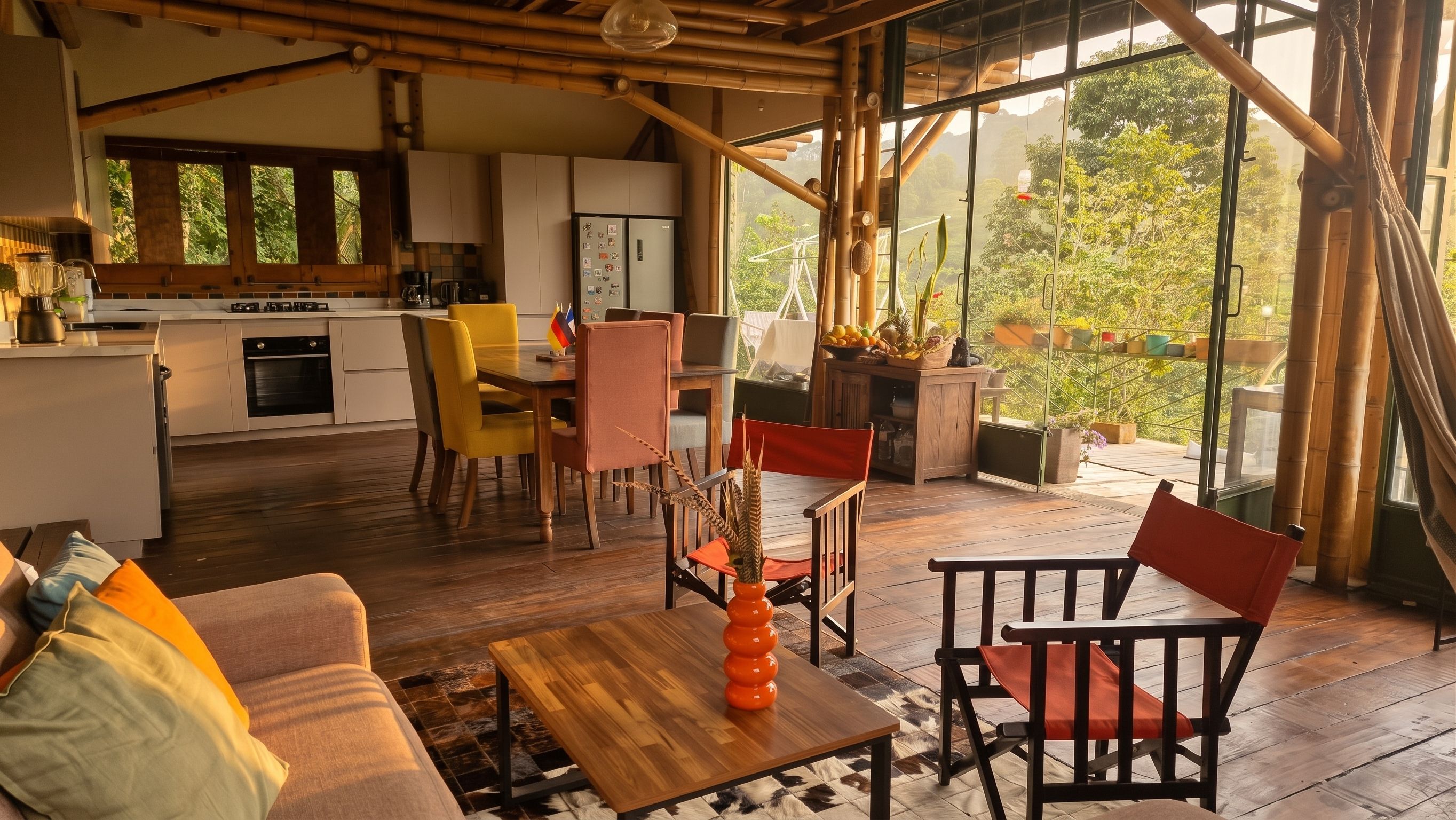 A modern interior with a dining area, kitchen, and large windows offering a view of greenery.