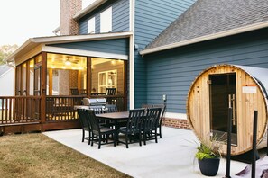 Un patio con tavolo e sedie in legno, una sauna e una zona coperta con una griglia.