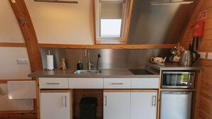 Una cocina compacta con un lavamanos, un microondas y un refrigerador pequeño. Tiene techo de madera y una ventana sobre el lavamanos.
