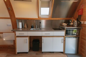 Una cocina compacta con un lavamanos, un microondas y un refrigerador pequeño. Tiene techo de madera y una ventana sobre el lavamanos.