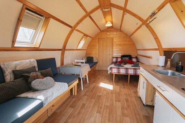 A cozy, compact room with a loft bed, a small dining table, a bench, and a kitchenette.