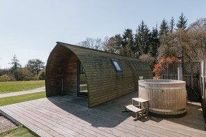Una estructura de madera con techo curvo y un jacuzzi en una terraza de madera.