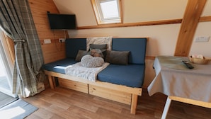 A cozy room with a wooden bed, a small table, a TV mounted on the wall, and a window with a view.