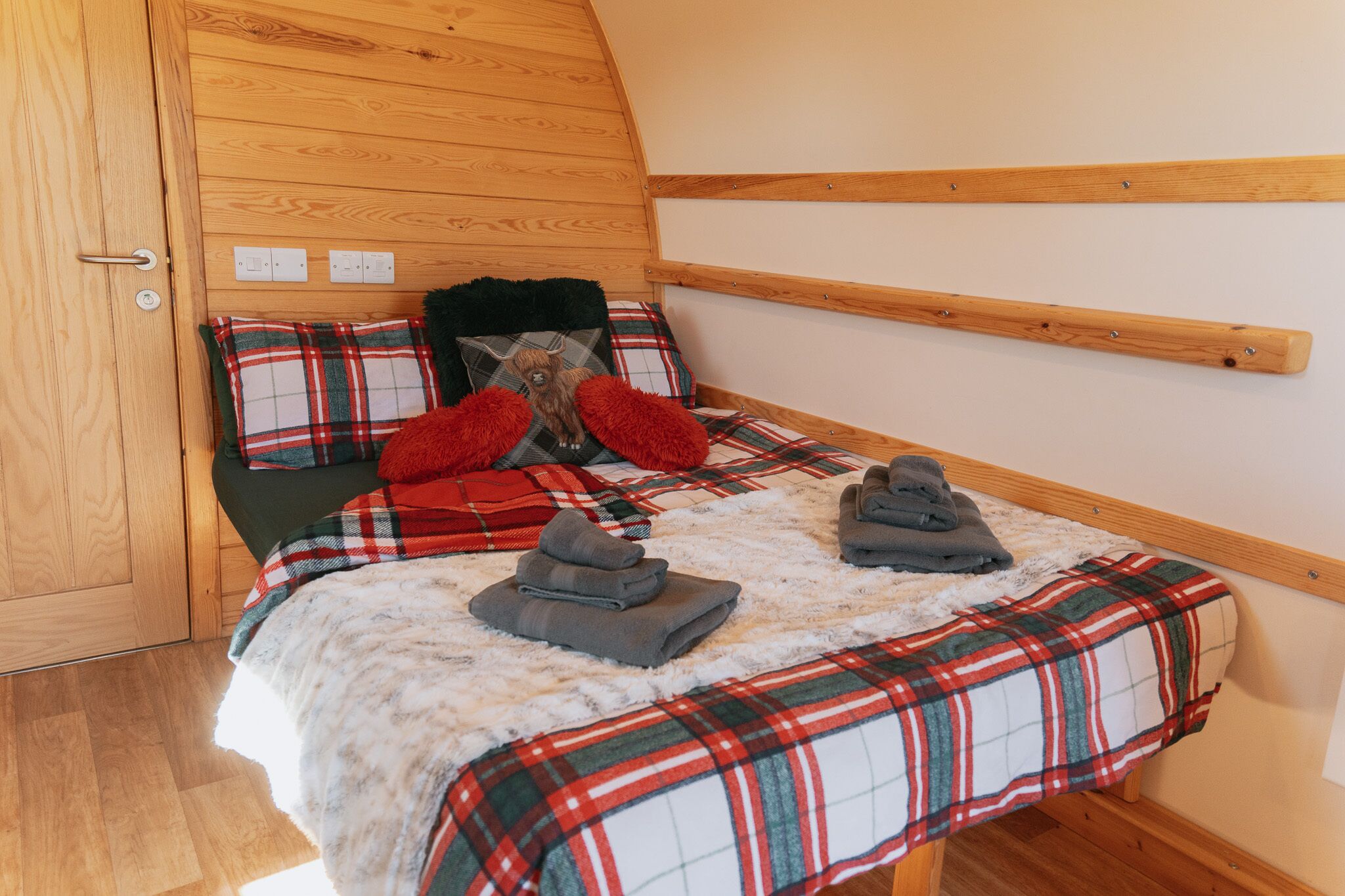 A cozy bedroom with a wooden ceiling, a plaid bedspread, and a fluffy white rug.