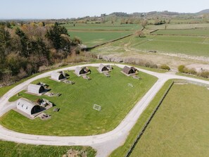 An aerial view of a rural property with multiple farmhouses, a central grassy area, and a surrounding road. - Cosy Rural Cabin with Private Hot Tub (Thirsk)