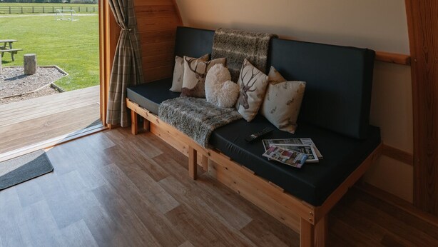 A cozy, wooden-framed room with a built-in bench and a view of a green field. - Cosy Rural Cabin with Private Hot Tub (Thirsk)