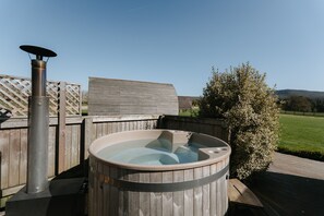 A hot tub with a wooden exterior, a metal heater, and a wooden deck. - Cosy Rural Cabin with Private Hot Tub (Thirsk)