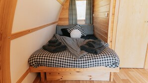 Une chambre de style « loft », avec un plafond en pente, un lit recouvert d’une couette à carreaux et une fenêtre agrémentée de rideaux.