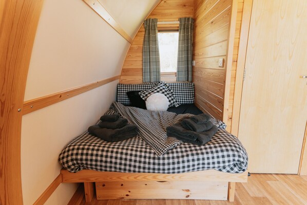 Une chambre de style « loft », avec un plafond en pente, un lit recouvert d’une couette à carreaux et une fenêtre agrémentée de rideaux.