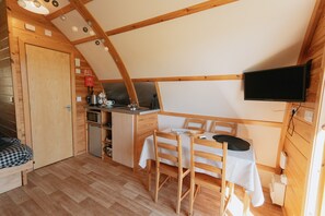Une pièce compacte comprenant un coin cuisine, un espace repas et un téléviseur fixé au mur.
