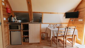 Une cuisine compacte équipée d’un micro-ondes, d’une bouilloire et d’un évier, ainsi qu’une table à manger avec des chaises et un téléviseur fixé au mur.