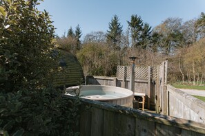 A wooden deck with a hot tub, surrounded by dense foliage and a wooden fence. - Cosy Rural Cabin with Private Hot Tub (Thirsk)