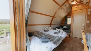 A cozy, rustic bedroom with a bed, a window, and a wooden door. - Cosy Rural Cabin with Private Hot Tub (Thirsk)