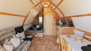 A cozy, compact living space with a lofted kitchen, a sofa with decorative pillows, and a dining area. - Cosy Rural Cabin with Private Hot Tub (Thirsk)