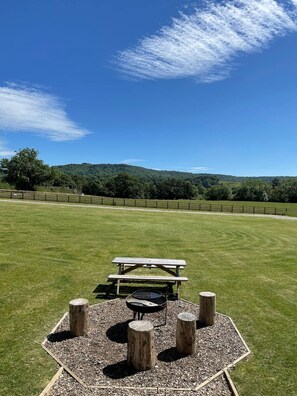 A picnic area with a table and benches, surrounded by a wooden fence and a grassy field with trees in the background. - Cosy Rural Cabin with Private Hot Tub (Thirsk)