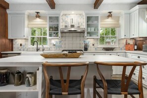 A kitchen with white cabinets, a central island with two wooden chairs, and a window overlooking greenery. - Red House Farm, an Historic Metamora MI Equestrian Estate (Metamora)