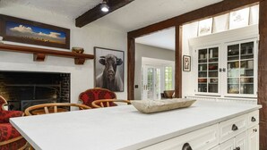 Een keuken met een groot kookeiland, witte kasten en een open haard. Er staan stoelen en er hangt een schilderij aan de muur.