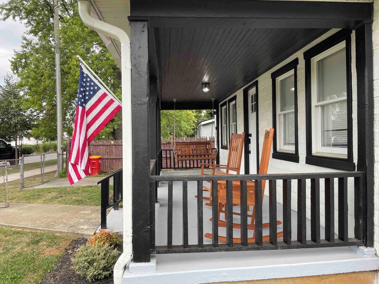 Une véranda avec une balustrade noire, une chaise berçante en bois et un mât sur lequel flotte le drapeau américain.