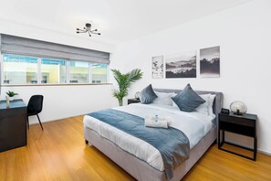 A modern bedroom with a bed, bedside tables, a desk, and a window.