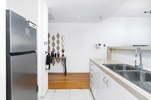 A modern kitchen with a stainless steel refrigerator, a wooden countertop, a double sink, and a small table with a mirror and a fire extinguisher. - Bloomfields Stylish 1BR in Al Raha Beach (Abu Dhabi)