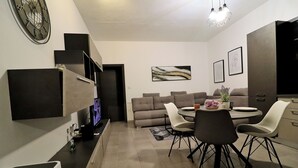 Ein modernes Wohnzimmer mit Essbereich, ausgestattet mit einer Sofagarnitur, einem Esstisch mit Stühlen, einem Fernseher und Kunstwerken an den Wänden.