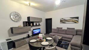 Ein modernes Wohnzimmer mit Essbereich, grauem Sofa, Flachbildfernseher und abstrakter Kunst an der Wand.