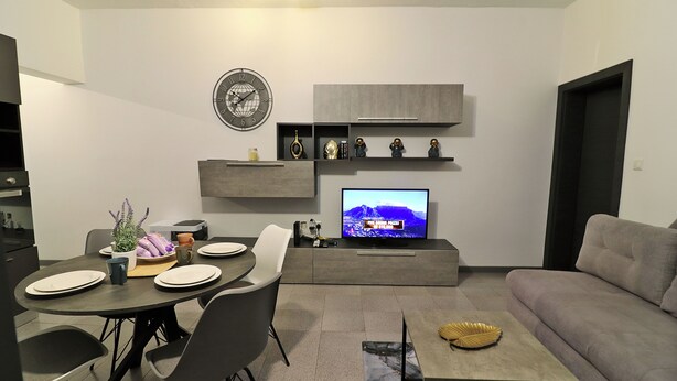 Ein modernes Wohnzimmer mit Essbereich, einem Flachbildfernseher und einem grauen Sofa.