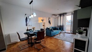 A modern living room with a blue sofa, a dining area with a table set for two, and a large window with curtains. - Apartment with self- check in, free private parking, WI-FI in brilliant Zagreb (Zagreb)