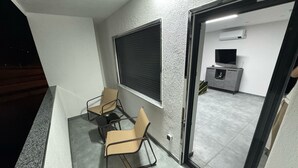 A balcony with two chairs and a table, a sliding door leading to a room with a TV and a cabinet. - Modern Apartments Gelsenkirchen highway A42 and A2 vacation apartment (Gelsenkirchen)