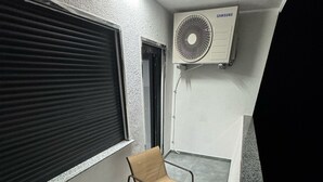 A small balcony with two chairs and a table, an air conditioning unit, and a window with blinds. - Modern Apartments Gelsenkirchen highway A42 and A2 vacation apartment (Gelsenkirchen)