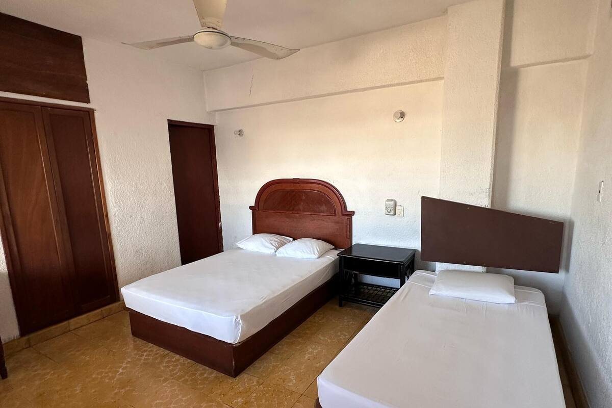 Une chambre d’hôtel avec deux lits simples, un ventilateur de plafond et une armoire en bois.