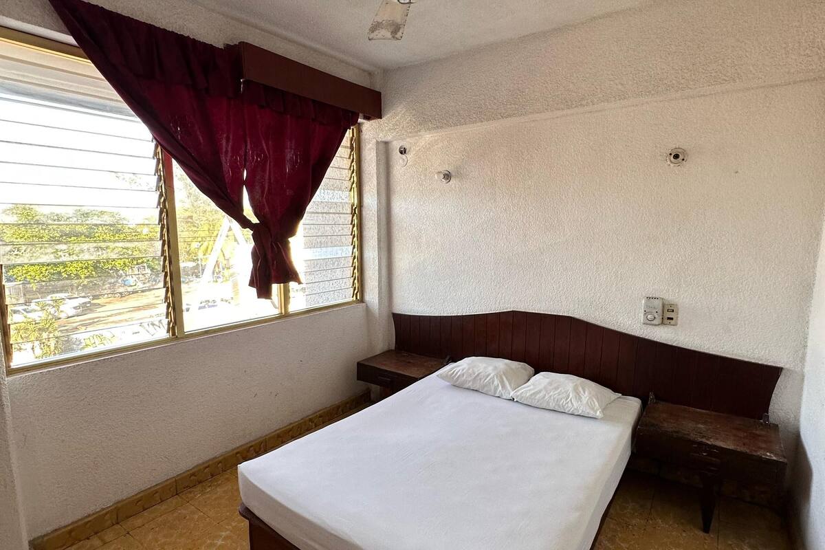 Une chambre à coucher avec un lit, un ventilateur de plafond, une fenêtre avec des rideaux et une vue sur l’extérieur.