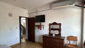 Una camera con un letto, una cassettiera, una sedia, un televisore e un condizionatore d'aria.