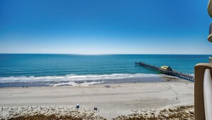 Ein Strand mit einem Steg, der ins Meer führt, feinem Sand und blauem Himmel.