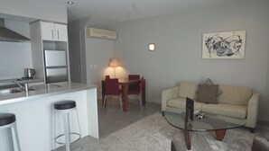 A modern kitchen with a built-in island, a dining area with a table and chairs, and a living room with a sofa and a coffee table. - Paihia Waterfront 1 Bedroom Apt & Pool (Paihia)