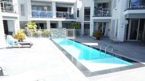 A swimming pool area with a tiled deck, lounge chairs, and a white fence. - Paihia Waterfront 1 Bedroom Apt & Pool (Paihia)
