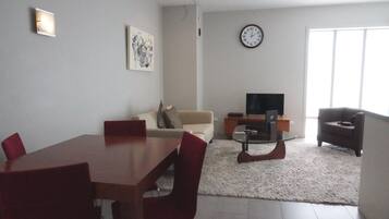 Una sala de estar moderna con una mesa de comedor, sillas rojas, un sofá, un televisor y un reloj en la pared.