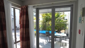 A room with a sliding glass door leading to an outdoor patio with a table and chairs. - Paihia Waterfront 1 Bedroom Apt & Pool (Paihia)