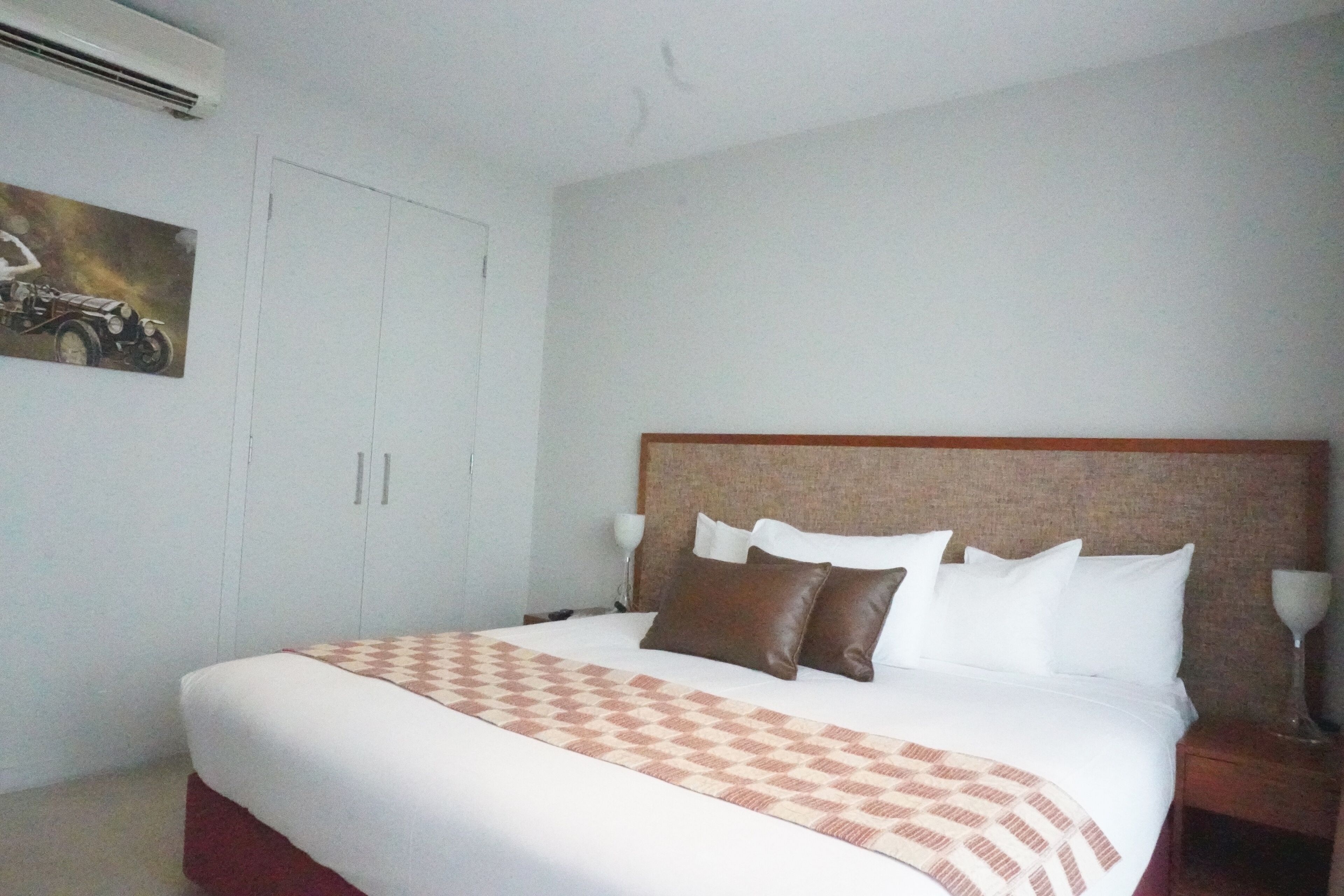 A hotel room with a large bed, a headboard, a nightstand, and a painting on the wall.