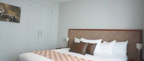 A hotel room with a large bed, a headboard, a nightstand, and a painting on the wall.