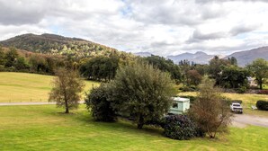 A rural landscape with a green field, trees, and a distant mountain range.